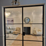 Double hinged glass door with black metal frame opening to modern living room with chandelier, armchairs, and fireplace