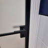 Modern hinged black metal frame door with frosted glass and black handle in tiled room