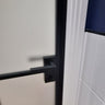 Modern hinged black metal frame door with frosted glass and black handle in tiled room