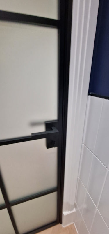 Modern hinged black metal frame door with frosted glass and black handle in tiled room