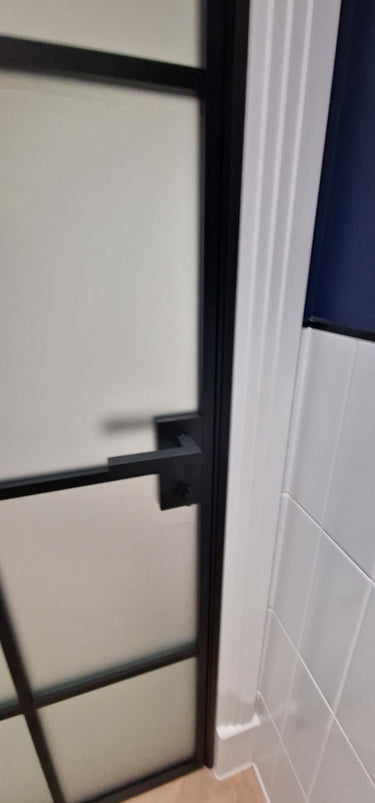 Modern hinged black metal frame door with frosted glass and black handle in tiled room