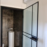 Modern bathroom with frosted glass hinged door, black frame, and tall white pedestal sink