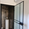 Modern bathroom with frosted glass hinged door, black frame, and tall white pedestal sink