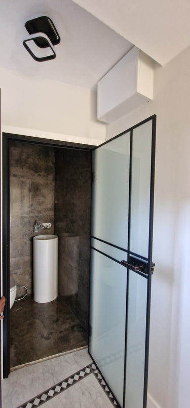 Modern bathroom with frosted glass hinged door, black frame, and tall white pedestal sink