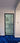 Modern hinged glass door with black metal frame and handle, set in white wall with blue carpet flooring