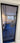 Black framed glass hinged door with handle reflecting a modern living room with blue carpet and furniture