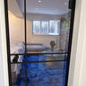 Modern hinged glass door with black frame opening to blue carpeted living room with sofa and round table
