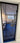 Modern black-framed hinged glass door opening to a living room with blue carpet and beige sofa