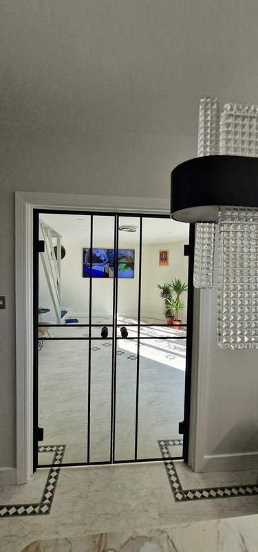 Modern interior with black double hinged glass doors, white walls, tiled floor, and chandelier