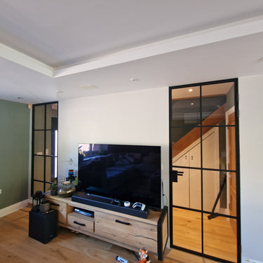 Modern living room with wooden TV stand, large flat screen TV, and black-framed glass hinged door