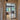 Modern black double hinged glass door with grid frame in beige hallway opening into dining area with wooden furniture and herringbone floor