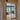 Modern black double hinged glass door with grid frame in beige hallway opening into dining area with wooden furniture and herringbone floor