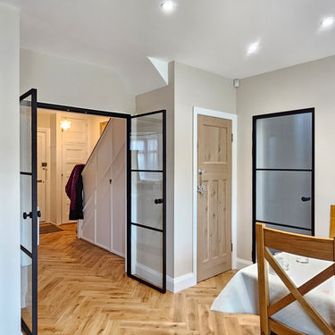 Interior view of modern home featuring black framed double hinged glass doors, wooden floor, and dining area