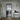 Modern interior with hinged glass door featuring black metal frame, leading to kitchen with herringbone wood floor