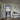 Modern interior with black framed hinged glass door leading to kitchen, wooden floor, console table with decor