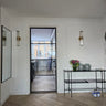 Modern interior with black framed hinged glass door leading to kitchen, white walls, console table with vases and flowers