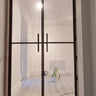 Double-hinged glass door with black metal frame in a white room under renovation