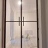 Double-hinged glass door with black metal frame in a white room under renovation