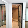 Interior view of hinged black-framed glass door leading to modern bathroom with beige tiles