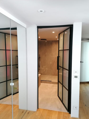 Interior view of hinged black-framed glass door leading to modern bathroom with beige tiles
