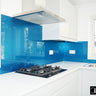 Modern kitchen with sparkling blue glass backsplash, white cabinets, gas stove, and stainless steel sink