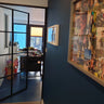 Interior view of a modern home office with a black-framed glass hinged door and a photo collage on a blue wall