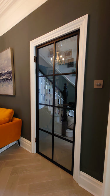 Modern black framed glass hinged door with white frame in home interior with orange couch