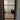 Black framed hinged glass door opening to room with wooden floor and black armchair with patterned cushion