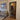 Modern living room with beige sofa, patterned cushions, black steel framed glass hinged door, and wall art