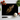 Black chopping board with golden feather print surrounded by cherry tomatoes, garlic, basil, and kitchen knife