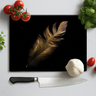 Black chopping board with golden feather print surrounded by cherry tomatoes, garlic, basil, and kitchen knife