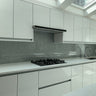 Modern kitchen with white cabinets, marble countertops, gas stove, gray backsplash, and dual sink under skylight