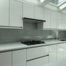 Modern kitchen with white cabinets, marble countertops, gas stove, gray backsplash, and dual sink under skylight