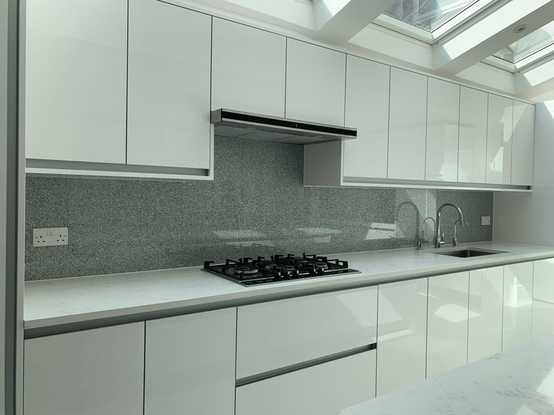Modern kitchen with white cabinets, marble countertops, gas stove, gray backsplash, and dual sink under skylight