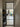 Black metal frame glass door opening to a modern kitchen with light wood floors and shoe rack