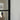 Black metal framed glass door hinge with blurred hallway and coats in the background