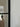 Black metal framed glass door hinge with blurred hallway and coats in the background
