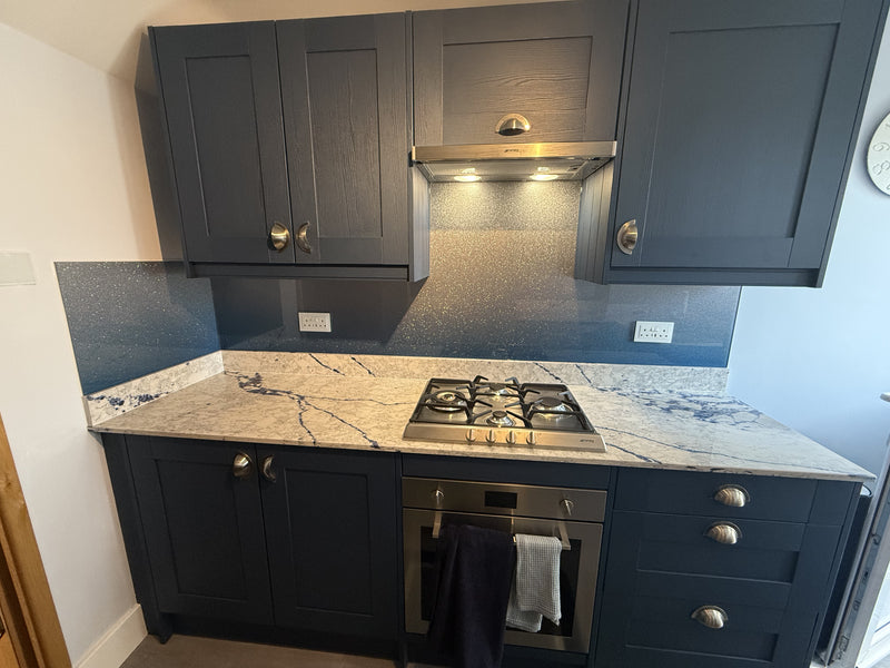 Modern kitchen with dark blue cabinets, marble countertop, gas stove, and glittery blue backsplash