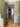 Modern black framed glass door in green-painted room opening to hallway with wood herringbone floor