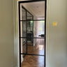 Black framed glass door with horizontal bars in modern hallway with herringbone wood floor and gray walls