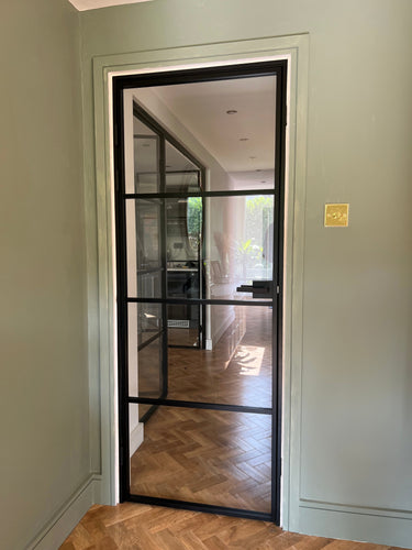 Black framed glass door with horizontal bars in modern hallway with herringbone wood floor and gray walls