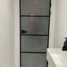 Modern black-framed frosted glass door in a minimalistic white bathroom with marble floor tiles and white sink