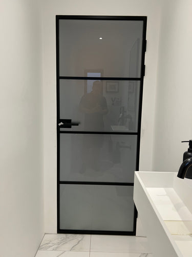 Modern black-framed frosted glass door in a minimalistic white bathroom with marble floor tiles and white sink