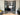 Modern double black metal frame glass doors with side panels opening to a living room with grey carpet and furniture