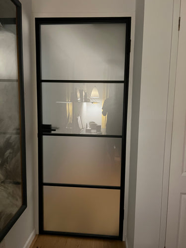 Black metal framed frosted glass interior door with home office seen through glass