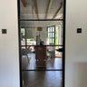 Black framed glass interior door showing a modern home with wooden furniture and outdoor garden view