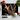 Black chopping board with orange lily print surrounded by cherry tomatoes, garlic bulb, basil, and kitchen knife