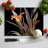 Black chopping board with orange lily print surrounded by cherry tomatoes, garlic bulb, basil, and kitchen knife