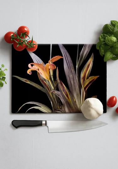 Black chopping board with orange lily print surrounded by cherry tomatoes, garlic bulb, basil, and kitchen knife