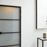 Modern interior with frosted glass hinged door framed in black metal, white walls, and abstract yellow art